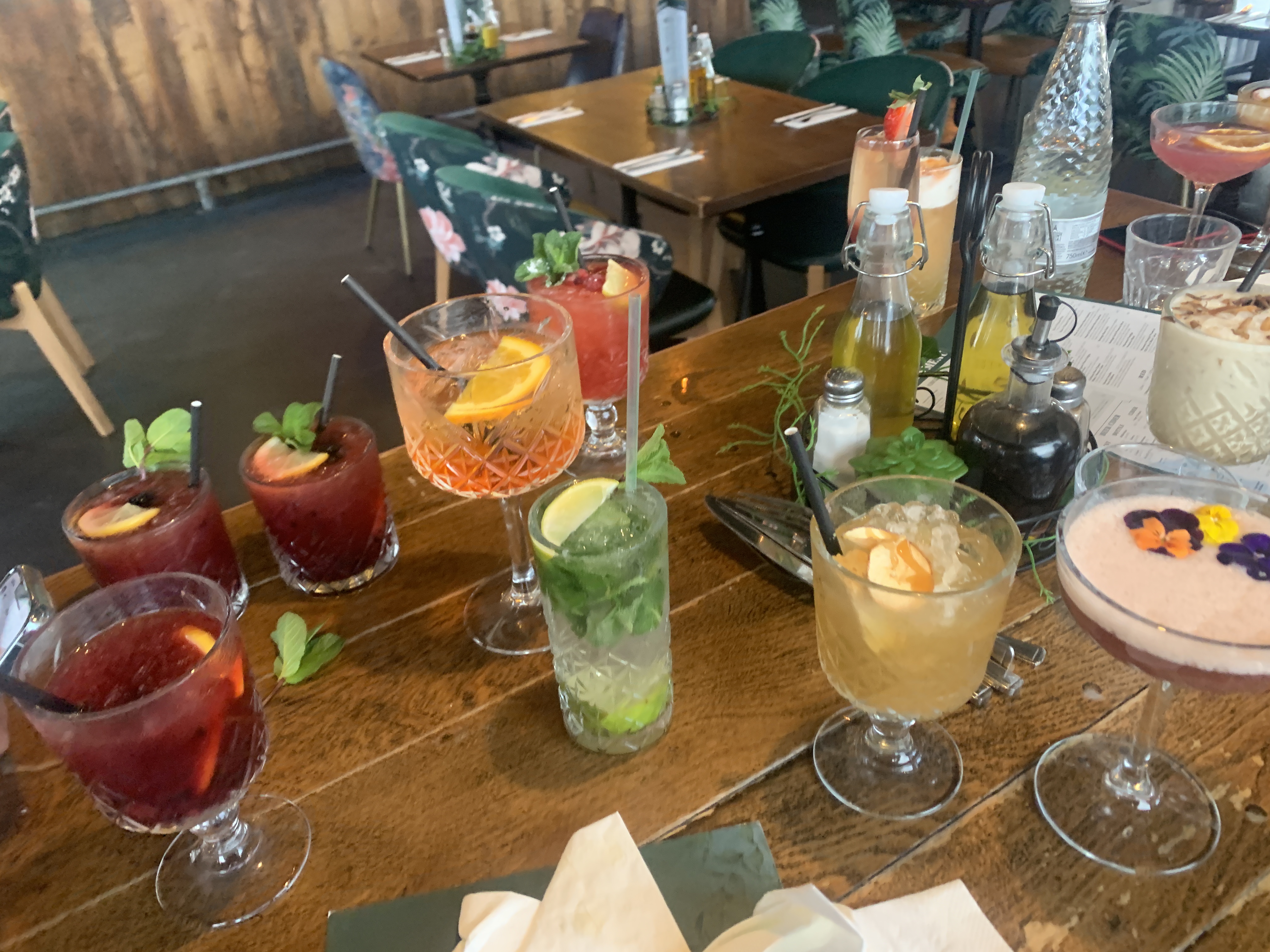 Assortment of colorful craft cocktails on wooden restaurant table including mojitos and specialty drinks