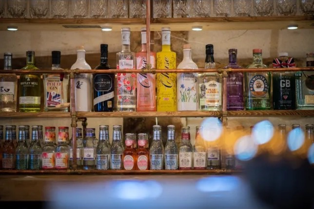 Premium gin collection display featuring colorful bottles including pink and yellow gins on wooden shelves