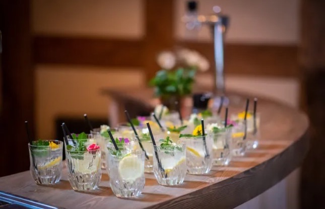 Elegant row of clear cocktails with edible flower garnishes on curved wooden bar