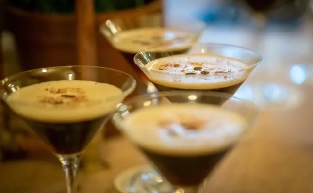 Three espresso martinis in coupe glasses with decorative foam art on wooden bar