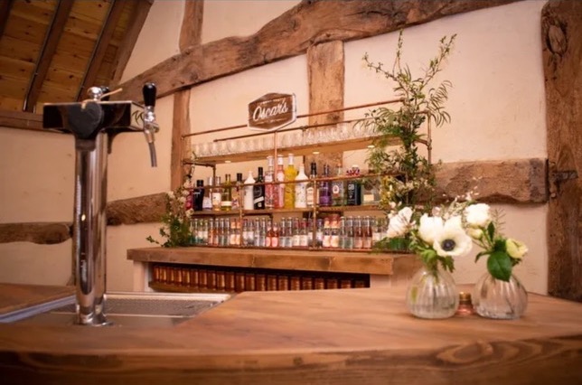 Mobile bar setup featuring draft beer tap, spirit collection, and elegant white flower arrangements