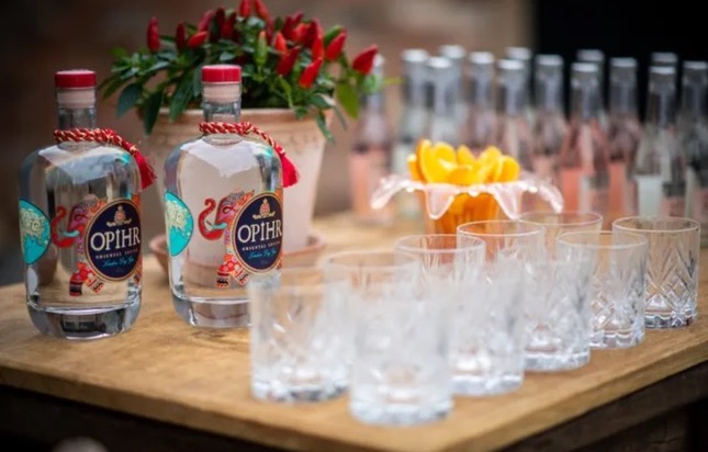 Opihr gin bottles with decorative packaging alongside crystal glasses and fresh flower arrangements