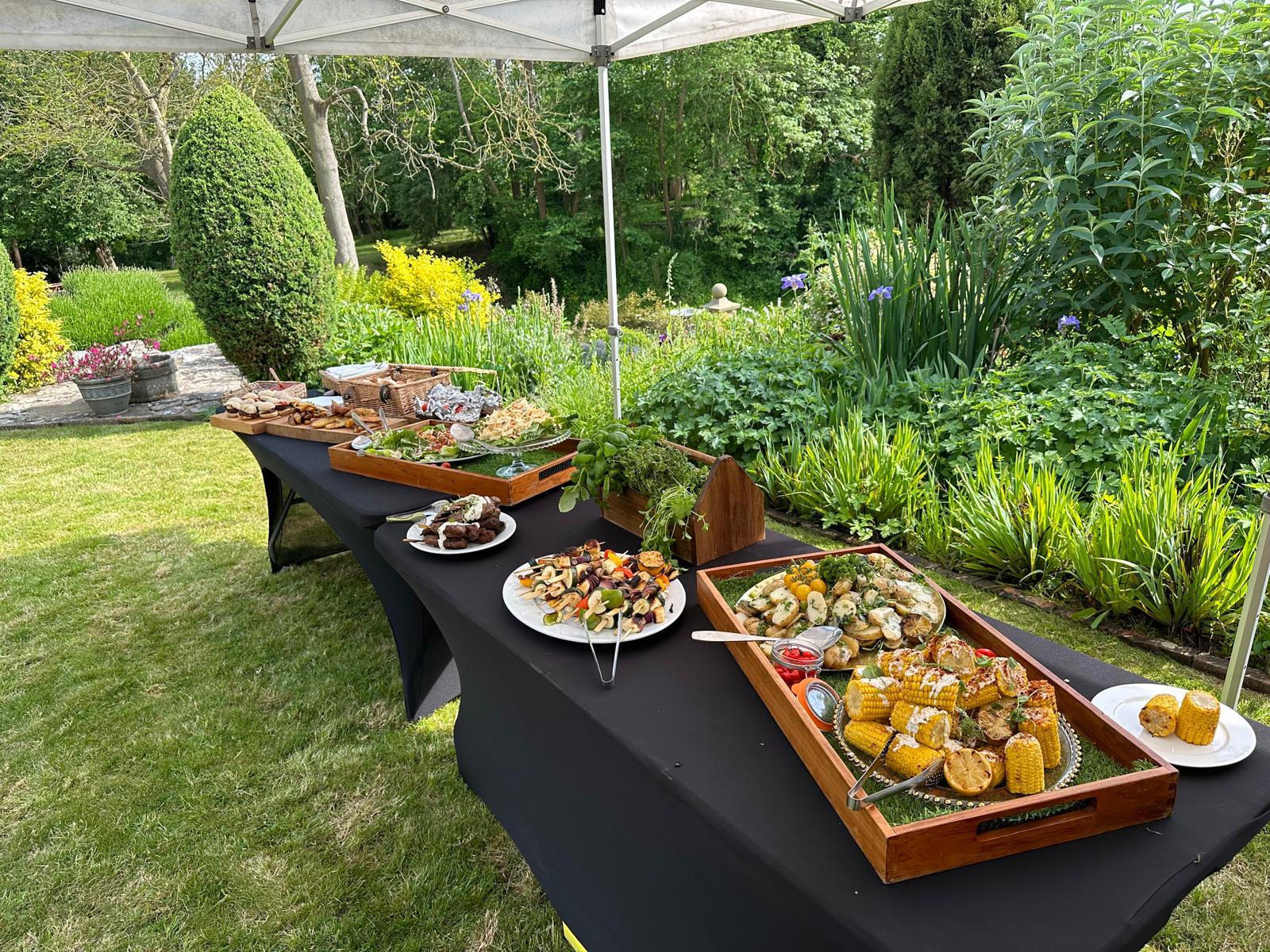 Outdoor catering buffet table with fresh produce, salads, and appetizers in garden setting