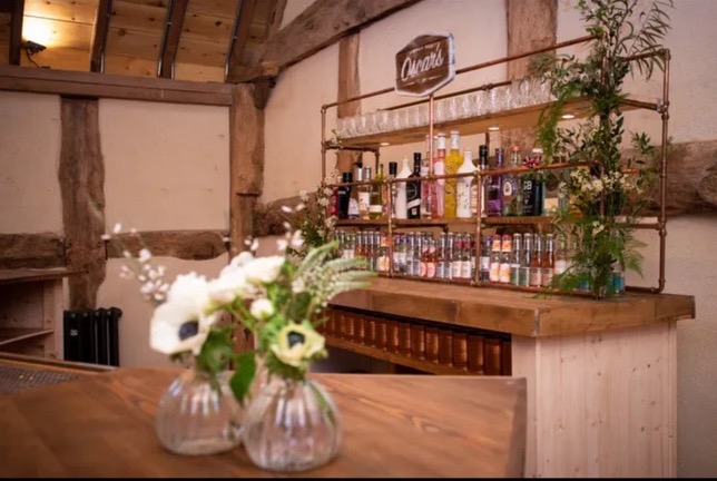 Rustic mobile bar setup in barn venue with exposed wooden beams and fully stocked spirit shelves