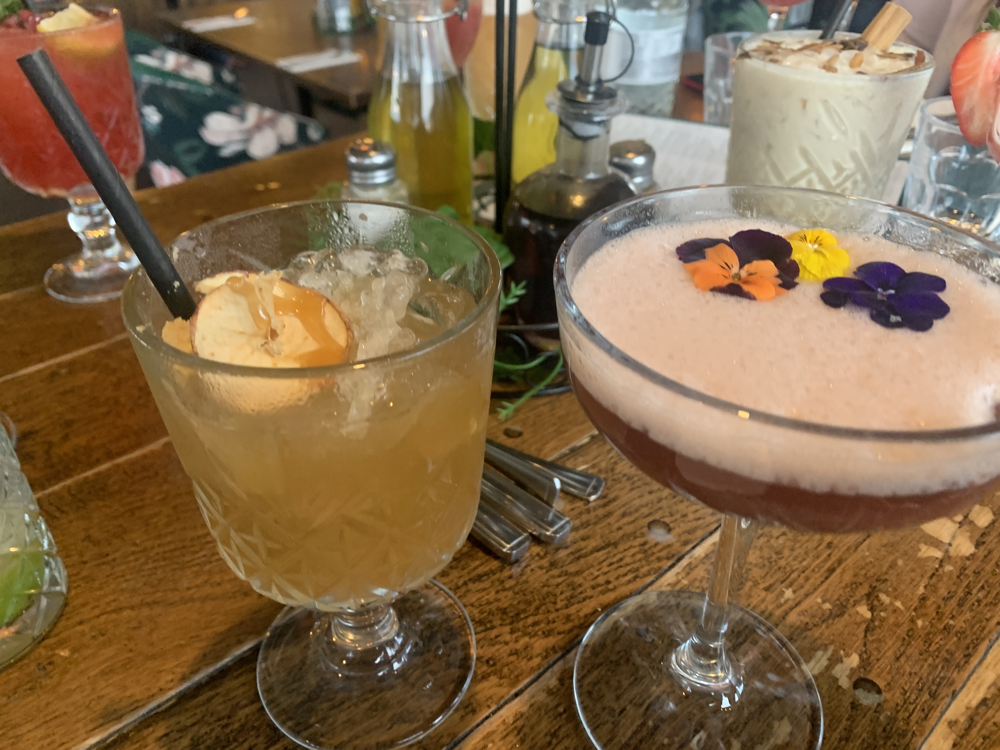 Two signature cocktails featuring golden drink with orange and pink foam cocktail with edible flower garnish